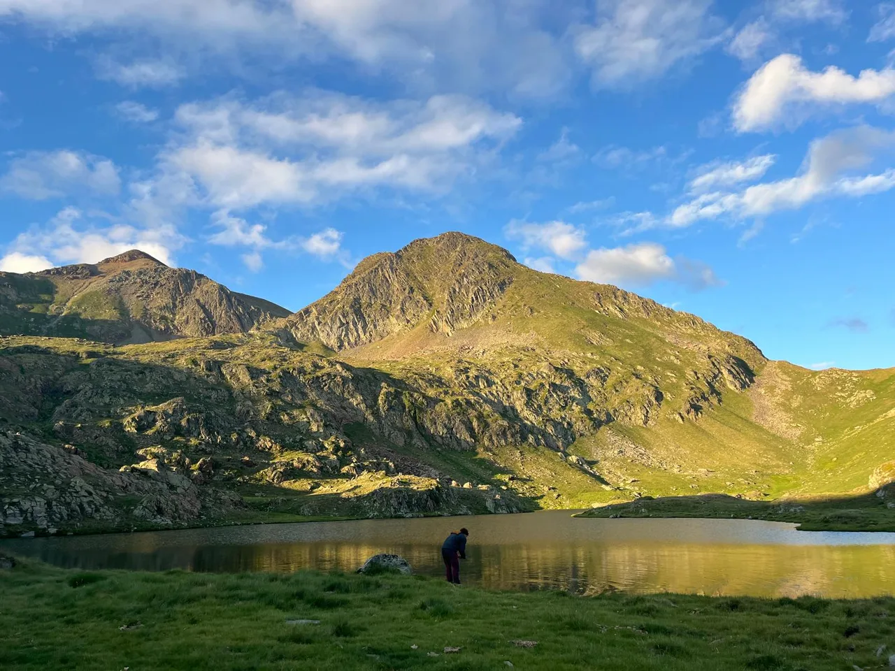 Un estany de muntanya sota cims coberts de prats verds