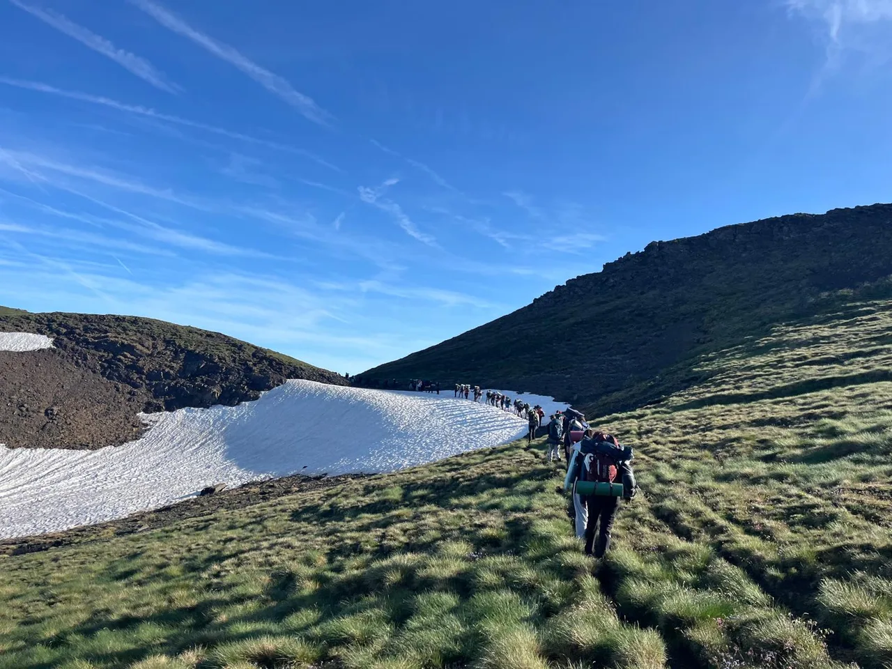Un excursionista puja per una congesta de neu entre prats