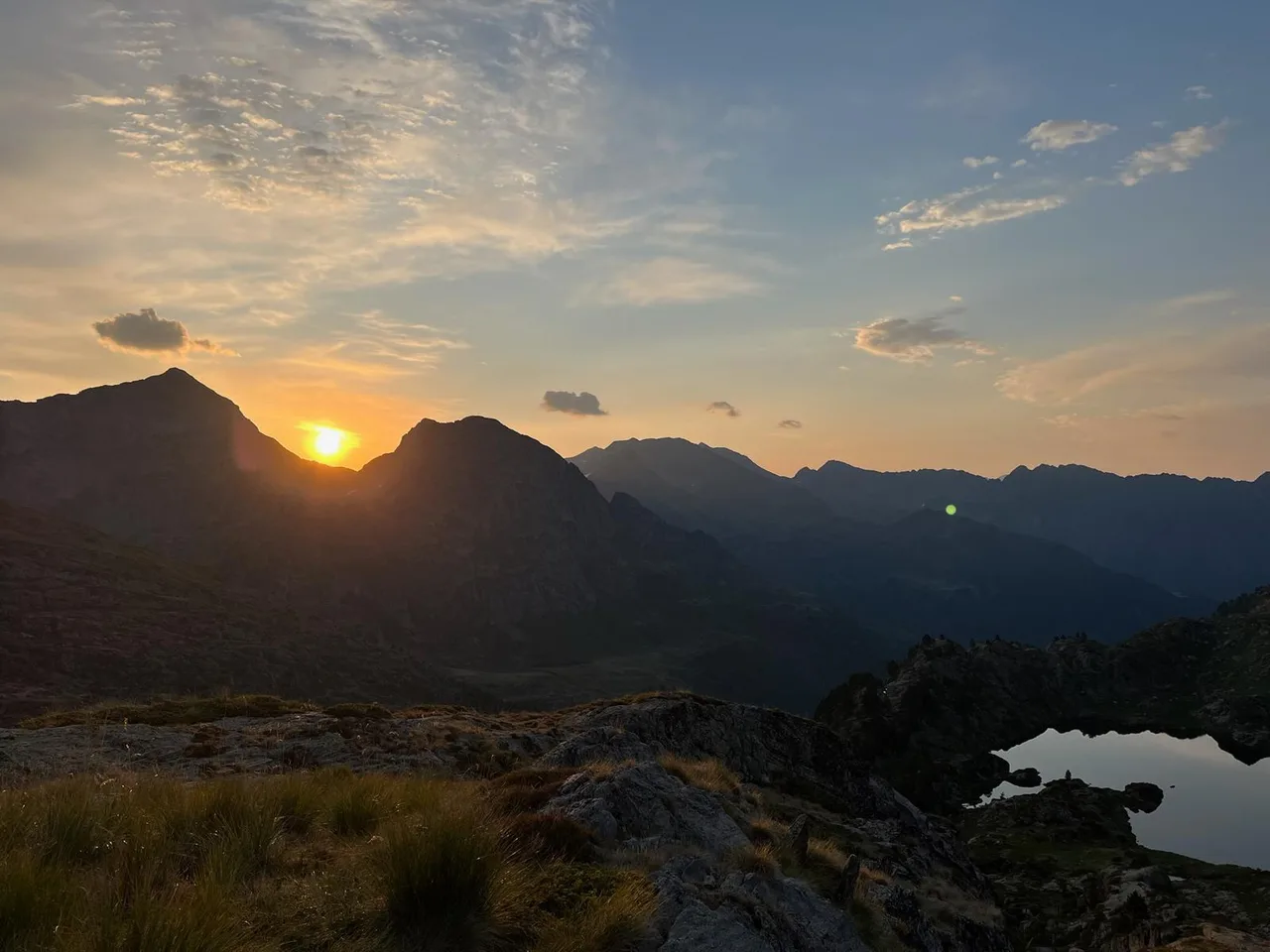 El sol es pon entre les muntanyes al costat d’un estany
